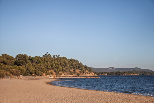 Coastal panorama at Plage de l'Argentiere at dusk, in la Londe, France, with a sandy beach, wooded Mediterranean shoreline and calm sea along the French Riviera in Provence.