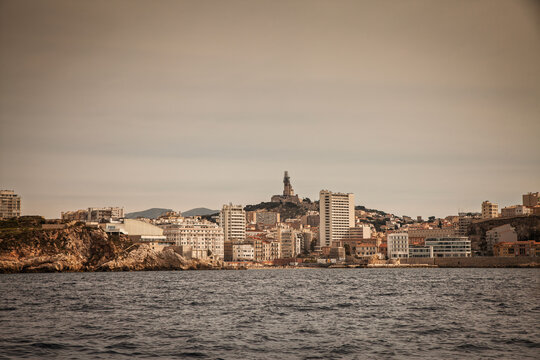 Scenic Mediterranean coastal view of the city skyline, with the sandy Plage des Catalans along the rocky shore and Basilique Notre-Dame de la Garde rising above the urban landscape in Marseille, Franc