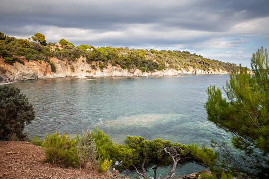 Panoramic view of the Mediterranean Sea and rocky, pine-covered coastline at Presqu'ile de Giens in Hyeres, Var, France, on the French Riviera, with clear coastal water beneath a dramatic cloudy sky.