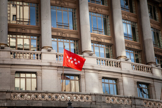 Flag of the Community of Madrid, comunidad de madrid, displayed in front of historic building facade in Madrid, Spain, the red regional banner with seven white stars, a symbol of autonomous community.