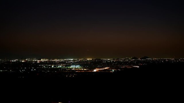 Night time lapse overlooking busy traffic and glowing city lights across the Phoenix metropolitan area on a clear winter evening in Arizona. Streams of vehicle lights capture rush-hour movement, commu