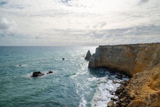 Scenic coastal cliff and rock formations with turquoise ocean waves crashing on the shore under blue sky