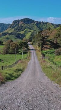 A scenic gravel road winds through green countryside and rolling hills in Waitomo, New Zealand, offering a peaceful rural travel landscape view.