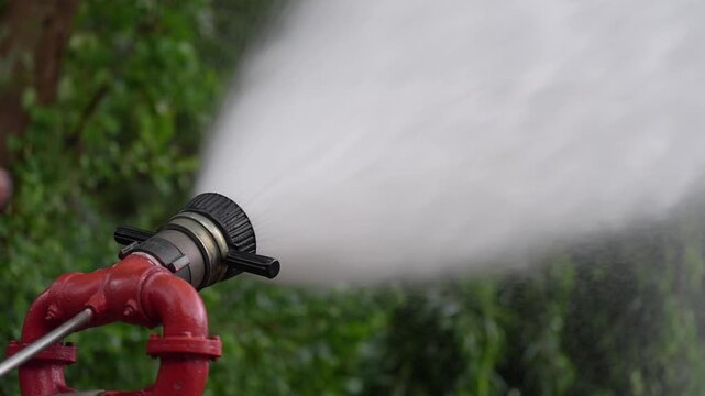 Fire hose nozzle water spray firefighting hydrant pressure emergency safety rescue equipment, high pressure mist and wide stream from red pipe valve and metal fitting during outdoor training drill