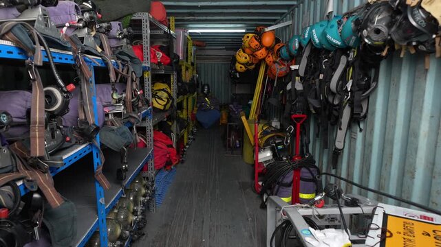 Storage container rescue equipment with helmet harness rope apparatus on shelf, warehouse corridor packed with safety gear and carabiner, organized inventory for emergency response training