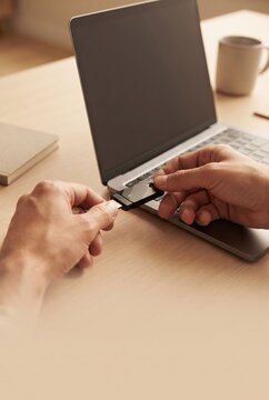Hands connecting USB security key to laptop on wooden desk