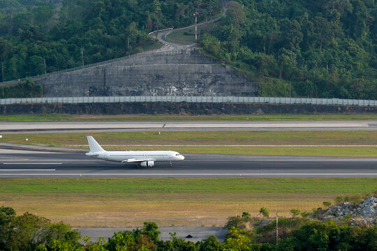 Passenger airplane take off on an airport runway with a prominent air traffic control tower visible on a lush green hill
