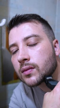 A young man trimming his beard with a trimmer in the bathroom. Close up