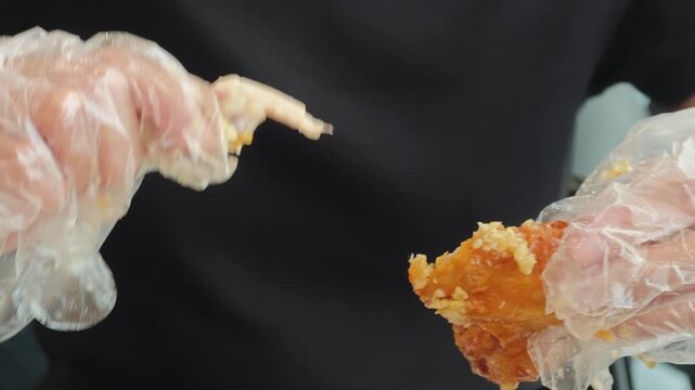 Young woman wearing disposable plastic gloves biting into a crispy garlic fried chicken wing, close up of her mouth and hands while eating
