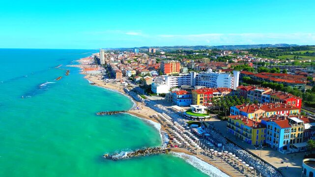 Revealing aerial pullback truck left pan left shot from Porto Recanati, vast Adriatic Sea expanses coming into full view, washing the sandy shore, complete with breakwaters, pastel-colored buildings
