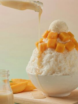 Sweet mango bingsu shaved ice dessert with condensed milk pouring on top