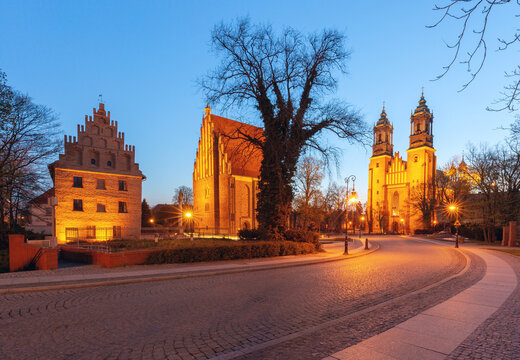 Illuminated historic architecture and cathedral towers on Ostrow Tumski in Poznan, Poland, during evening blue hour.