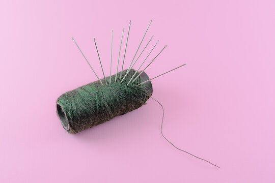 Green thread and needles isolated pink background 