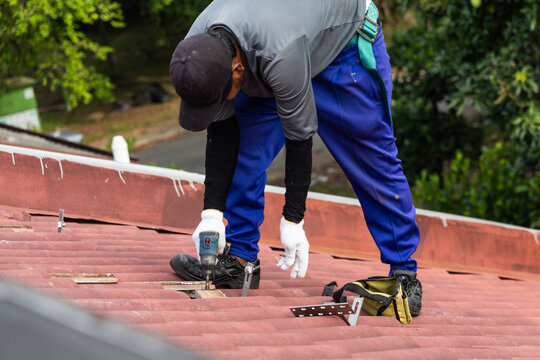 Closeup of of worker installing metal brackets onto house roof truss to prepare for solar photovoltaic or PV panels installation onto red rooftop of residential house in Malaysia