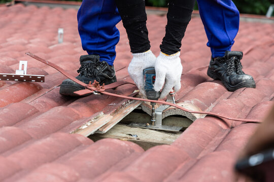 Closeup of of worker installing metal brackets onto house roof truss to prepare for solar photovoltaic or PV panels installation onto red rooftop of residential house in Malaysia