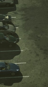 Several cars are parked in a lot with clear visibility of their shapes. The sunlight creates noticeable shadows on the ground. The scene shows a typical urban parking area.