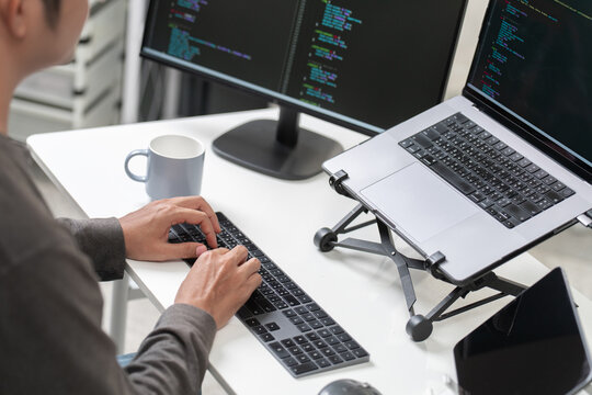 Modern workplace with computer coding on dual screens, keyboard, and smartphone
