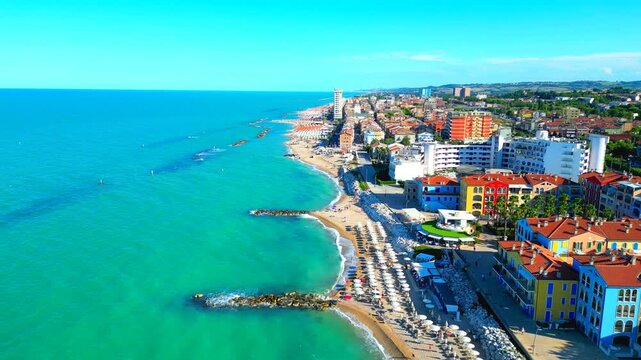 Splendid aerial truck left shot of Porto Recanati, from the shoreline to the deeper waters of the Adriatic Sea, vast wavy expanses sitting beside the sandy beach, with breakwaters, parasols, buildings