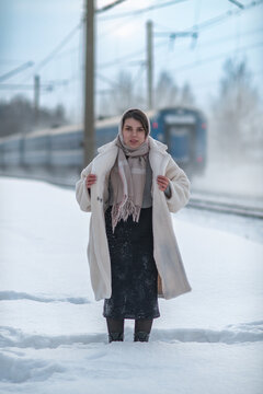 Young beautiful woman in winter outfit posing outdoors at a snowy railway station with a train on background.