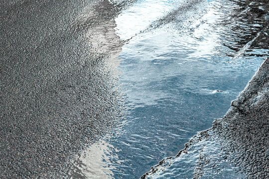 reflection of white clouds and blue sky in a puddle on wet asphalt.