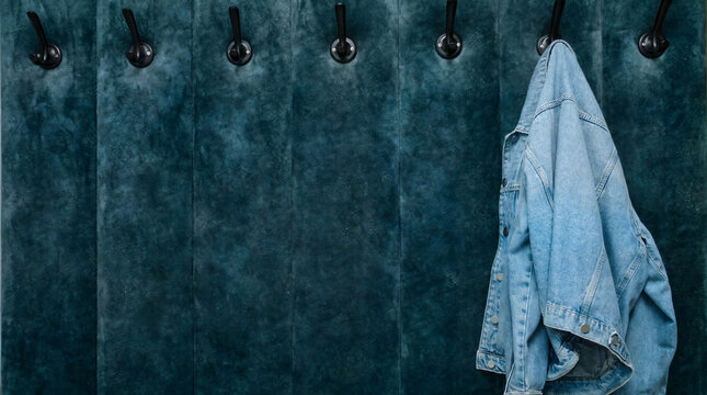 Denim jacket hangs gracefully from a hook on a plush teal velvet wall panel in a stylish modern hallway.