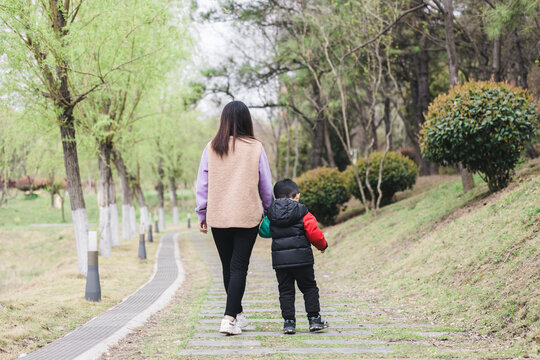 A woman and a young child walk side by side along a paved park path surrounded by spring greenery.