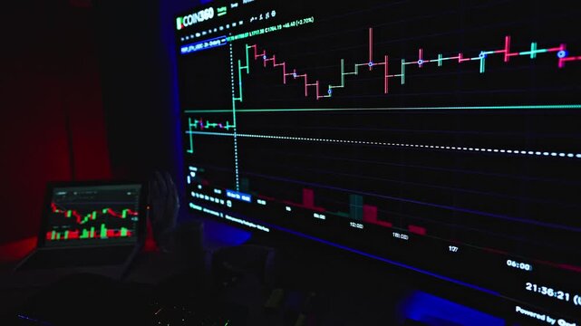 Businessman hand points toward a glowing computer monitor that displays complex financial trading charts and data visualizations during a high stakes session of analyzing volatile market movements.