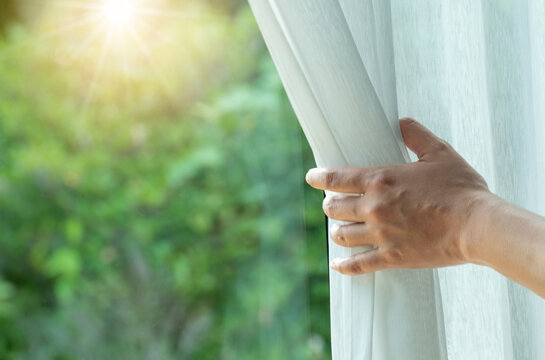 woman's hand She opened the curtains on the window. There was morning light through the window in her room, looking at the view of the mountains and trees as the sun rose.
