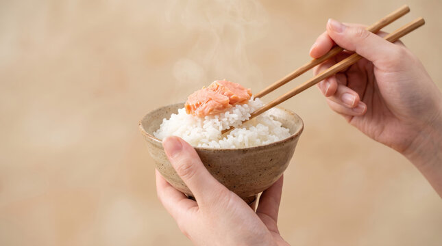 湯気が立つ炊き立ての白米にほぐし鮭をのせて箸で食べる手元 和食の食事風景