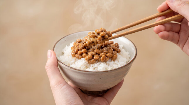 納豆ご飯を箸で持ち上げる手元 糸を引くねばねばの納豆と温かい白米 和食朝食素材