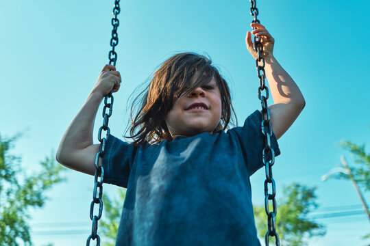 Boy on a playground swing looking toward the camera from below