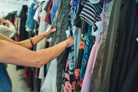 Hand reaching through a rack of colorful dresses at a thrift store