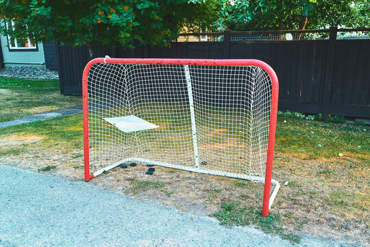 Red hockey net in a backyard with pucks on the ground