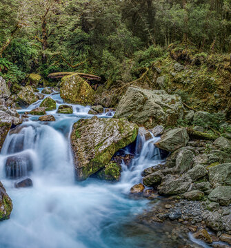 The Chasm, tuerkisfarbenes Wasser des Cleddau River zwischen bemoosten Felsbrocken, Holzsteg und Aussichtsplattform im Hintergrund, Milford Road, Fiordland National Park, Suedinsel, Neuseeland