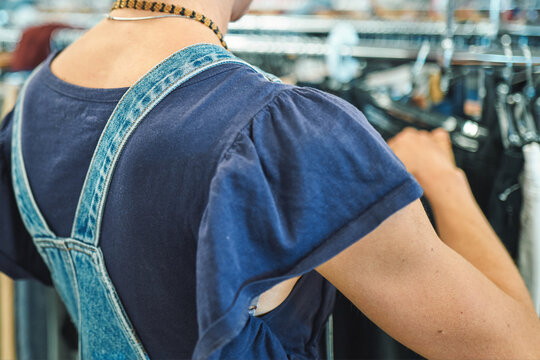 Woman in denim overalls reaching through a clothing rack from behind