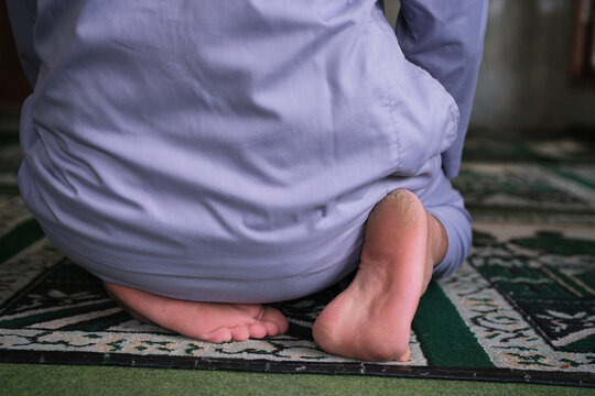A rear view of an Asian man performing the *tahiyat* (sitting) posture during prayer inside a mosque&mdash;one of the movements in the Islamic act of worship. Suitable for themes related to the Hijri New Ye