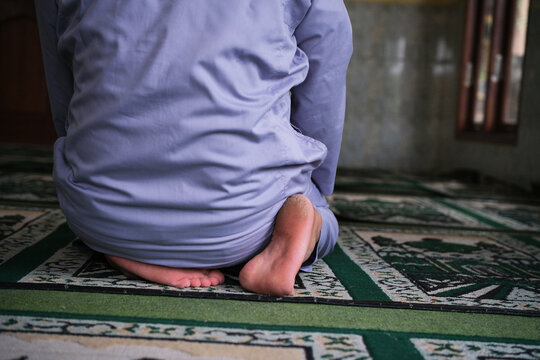 A rear view of an Asian man performing the *tahiyat* (sitting) posture during prayer inside a mosque&mdash;one of the movements in the Islamic act of worship. Suitable for themes related to the Hijri New Ye