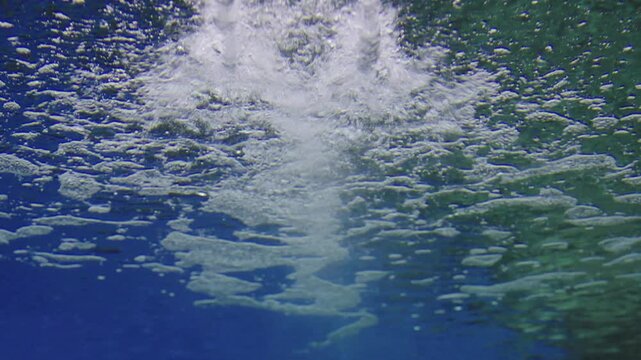 Underwater view looking up at the bright blue water surface. White bubbles and foam create a textured pattern against the light. Clean, refreshing, and dynamic aquatic background for summer themes.