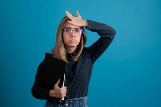 Frustrated Young Businesswoman Holding Folder on Blue Background .Anxious professional office worker woman making face expression holding black document organizer folder 