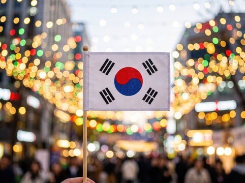 Small south korean flag held on a wooden stick against a blurred city street background with colorful bokeh fairy lights at night