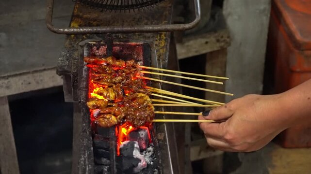 Hot glowing charcoal coals burning inside a traditional metal grill stove, producing smoke and bright flames for cooking street food.