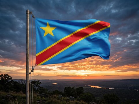 The national flag of the democratic republic of the congo waving on a metal flagpole against a dramatic sunset sky with clouds over a dark landscape horizon