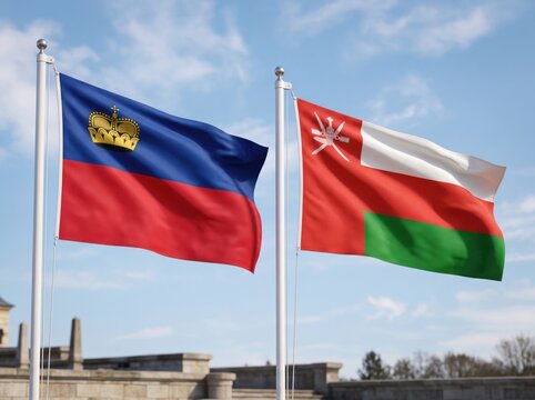 The national flags of liechtenstein and oman waving side by side on metal poles against a bright blue sky with light clouds above a stone architectural structure in the background