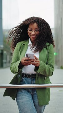 Young happy confident business woman standing on city street using mobile phone app