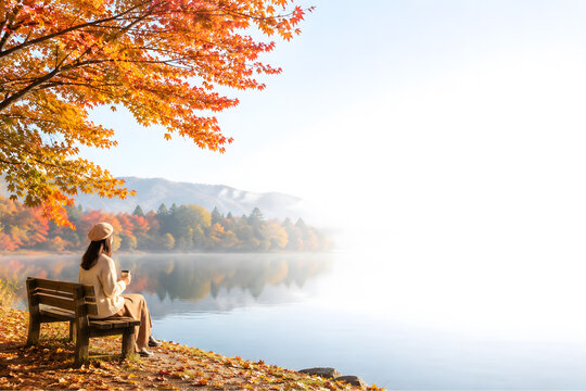 紅葉した木々と湖を眺めながらベンチで過ごす女性