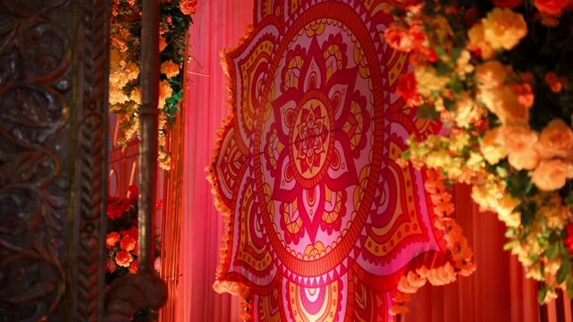 Close-up of colorful traditional Indian wedding decor featuring an ornate mandala pattern, floral arrangements, and warm ambient lighting. red, pink, orange, and gold details at wedding celebration 