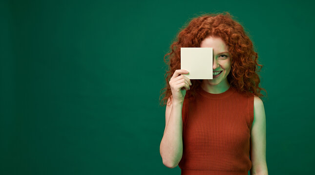 Cheerful redhead holding blank white card wearing colorful striped top