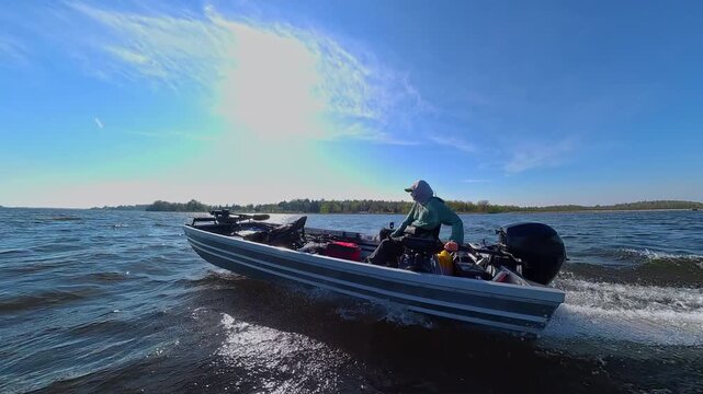 Small power boat speeding along the surface of the North American lake. Fishing boat with outboard motor floats on the water waves in the lake creating wake and white foamy trace.