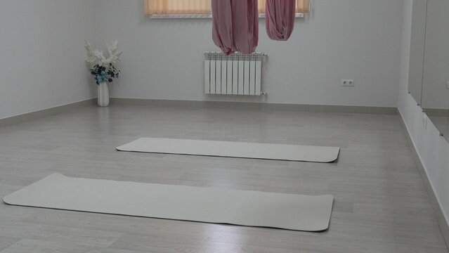 White yoga studio interior featuring two mats on the wooden floor and pink aerial silks hanging from the ceiling.