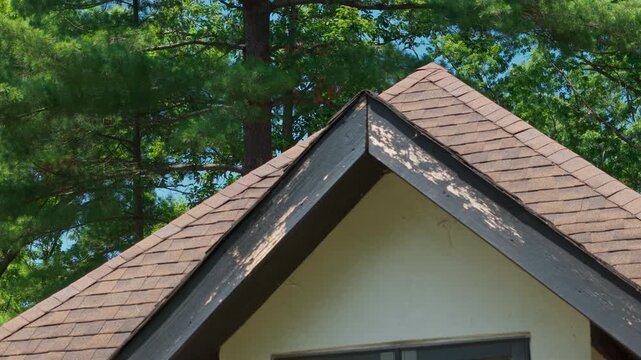 Residential roof gable with weathered wooden fascia and trim showing peeling paint and exterior wear. Damaged roof